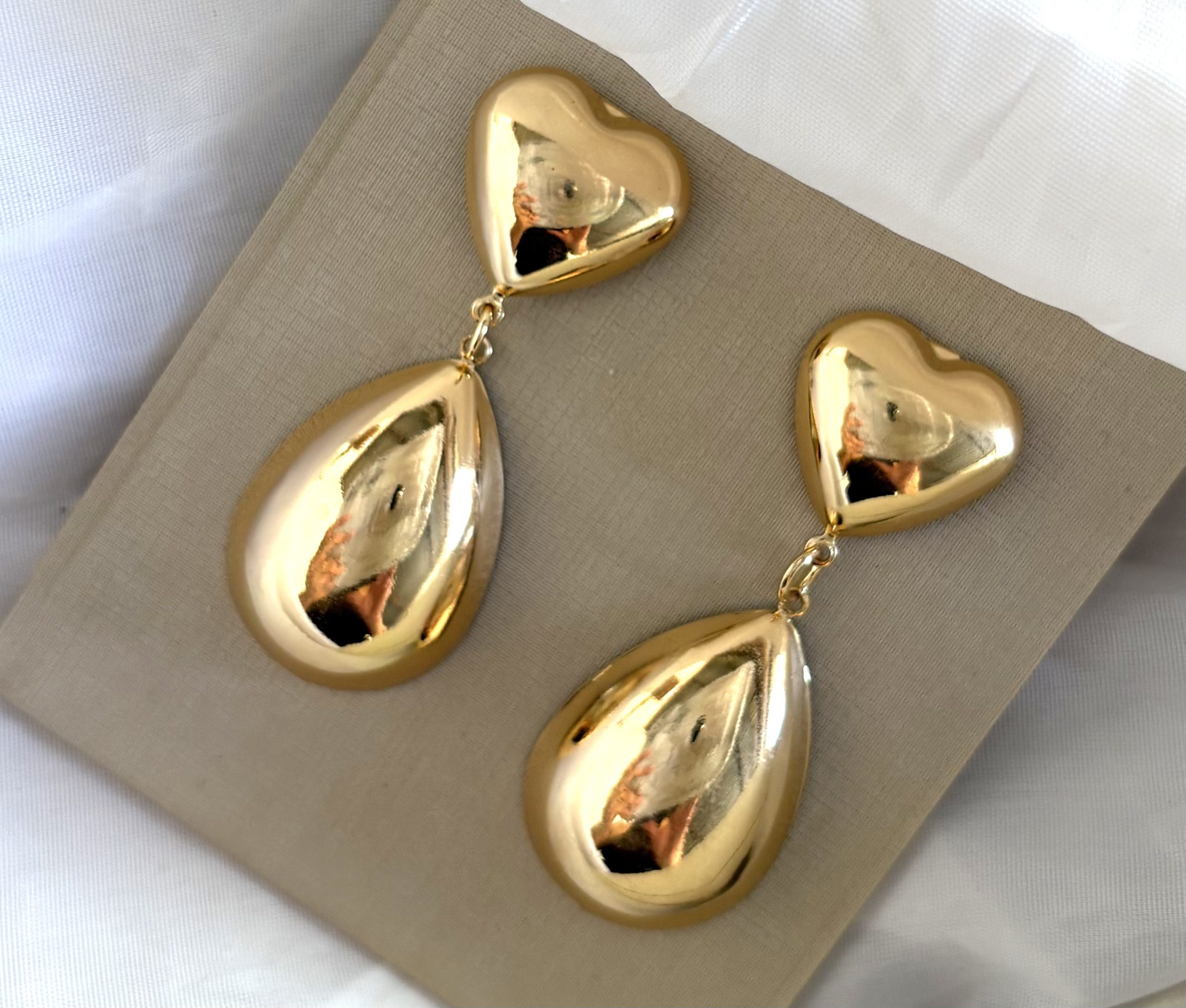 Brinco formato de coração na parte superior com uma gota alongada pendente.