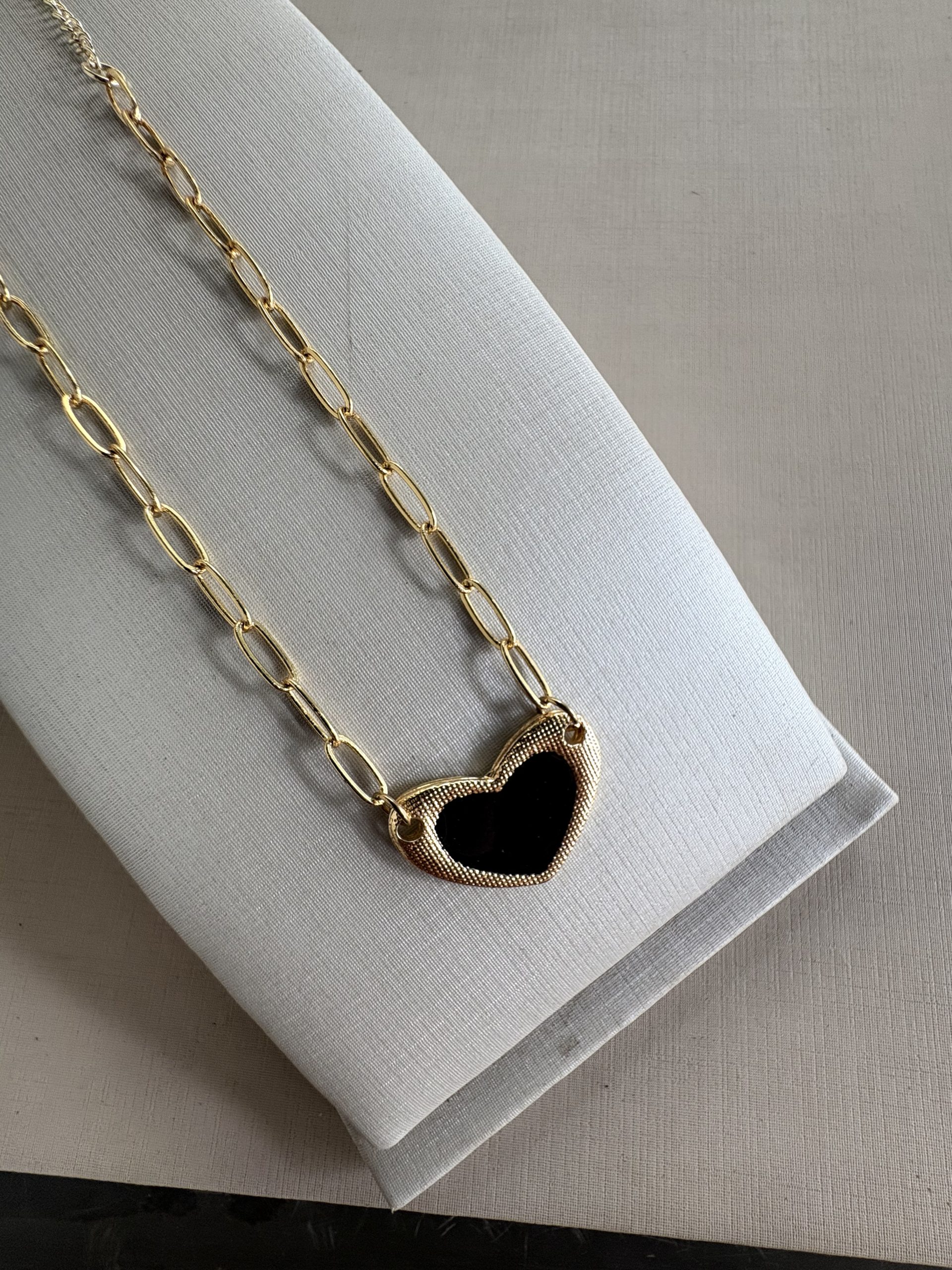 Colar coração dourado com detalhe preto.